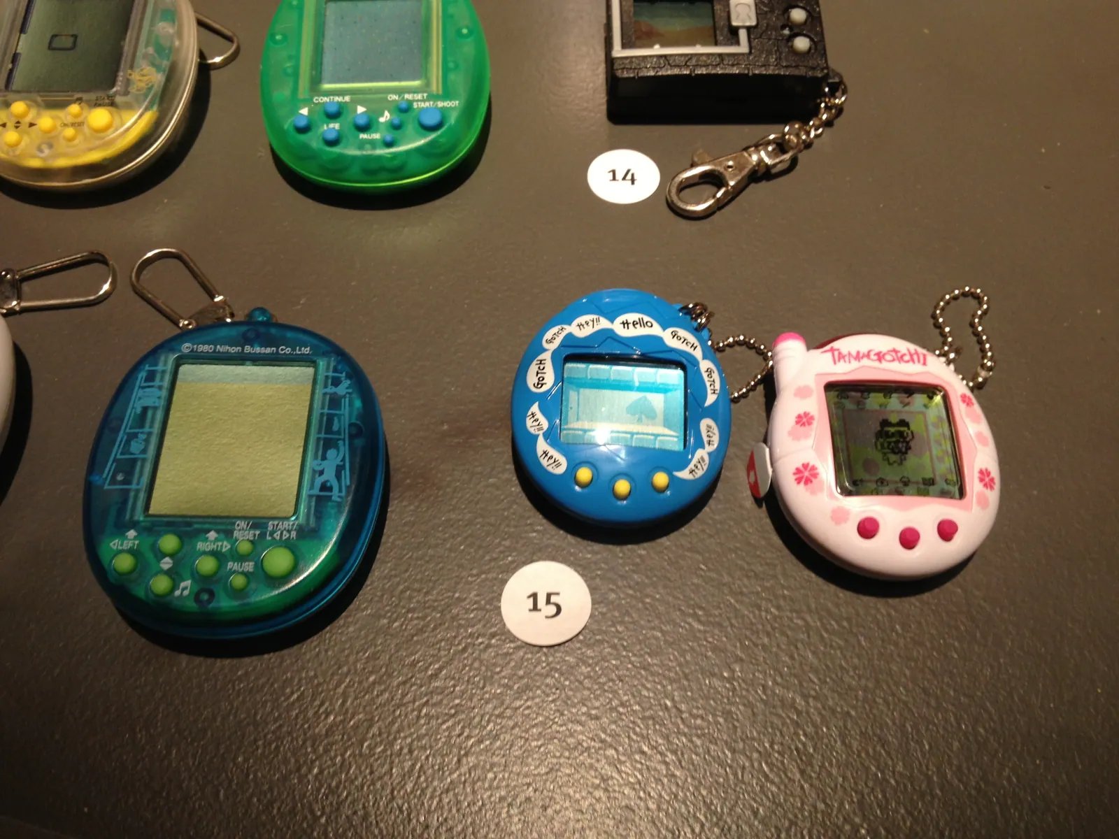 A numbered museum display containing several handheld virtual pets, including blue and pink Tamagotchi devices.
