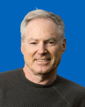 Head-and-shoulders portrait of Eric Horvitz, the Microsoft Research scientist who led the Lumière project, smiling in a dark sweater against a bright blue background.